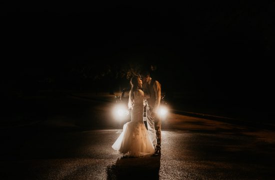 Wedding couple standing in front of car headlights